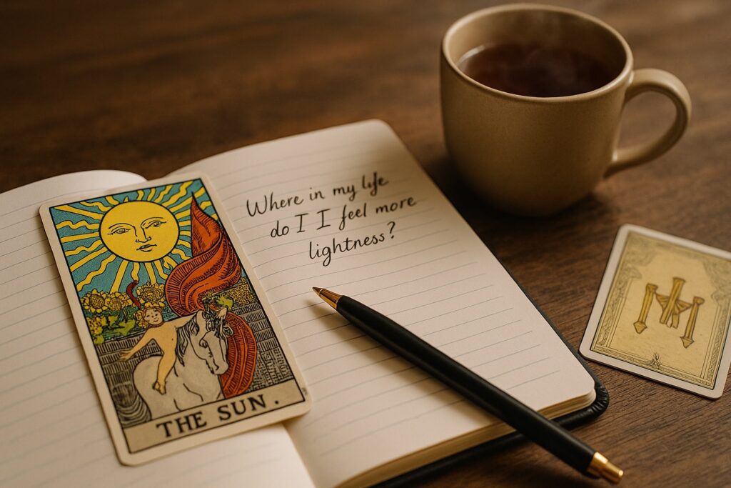 Tarotkarte „Die Sonne“ auf Notizbuch mit Frage „Where in my life do I feel more lightness?“, Stift, Teetasse.